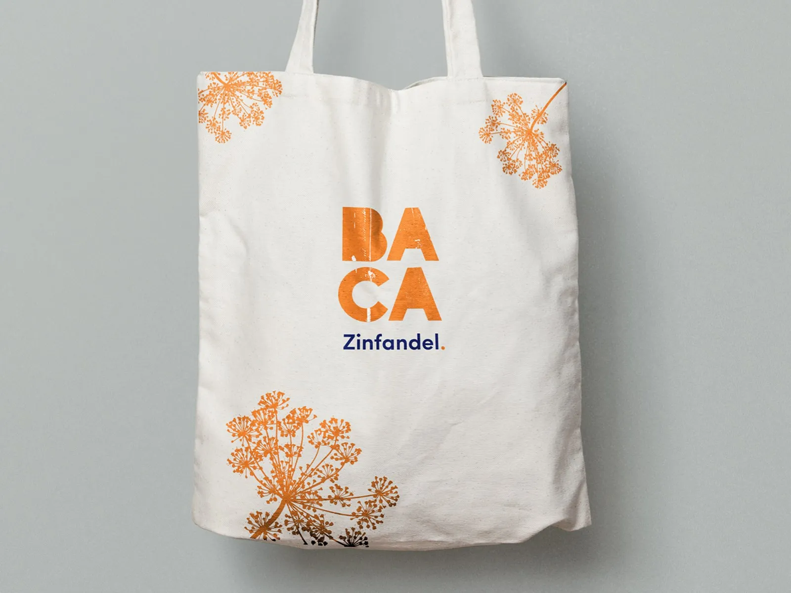 A cream canvas tote printed with the stacked BACA mark and an orange botanical pattern