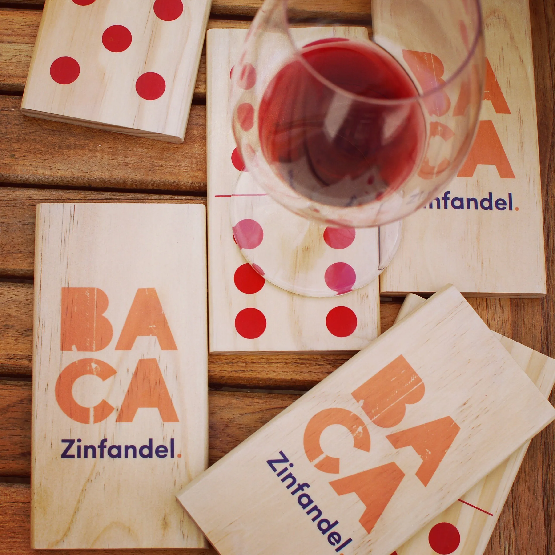 Custom wooden dominoes and game boards branded with the BACA mark, beside a glass of red
