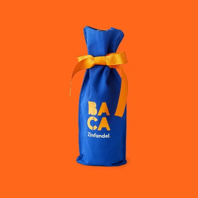 A cobalt BACA bottle bag tied with an orange ribbon, on orange